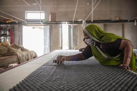 A person in a green head scarf working on a table

Description automatically generated